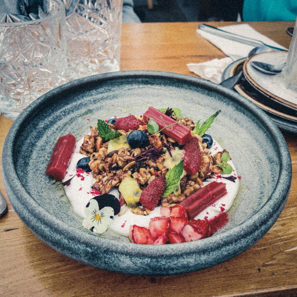 pexels-photo-765548-765548 A vibrant breakfast bowl with granola, strawberries, mint, and yogurt on a wooden table.